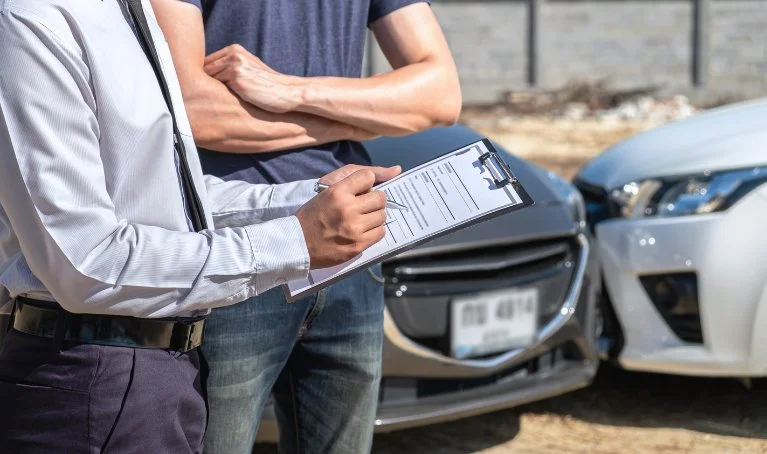 Car accident lawyer filling out legal documents at the accident scene with two damaged vehicles in the background